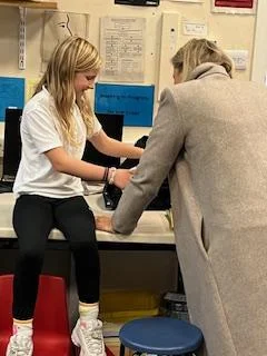 A smiling young girl and a supportive staff member working together at a desk during a Pitmedden Primary School club session, representing the journey of Community Link Childcare since 2000.