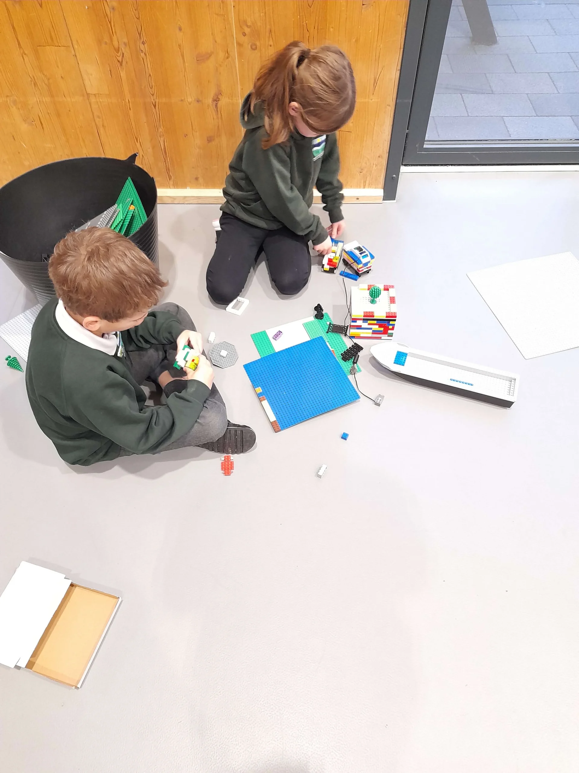 Two children in school uniform sitting on the floor and playing creatively with Lego building blocks at the Milltimber Primary School after school club in Aberdeen.