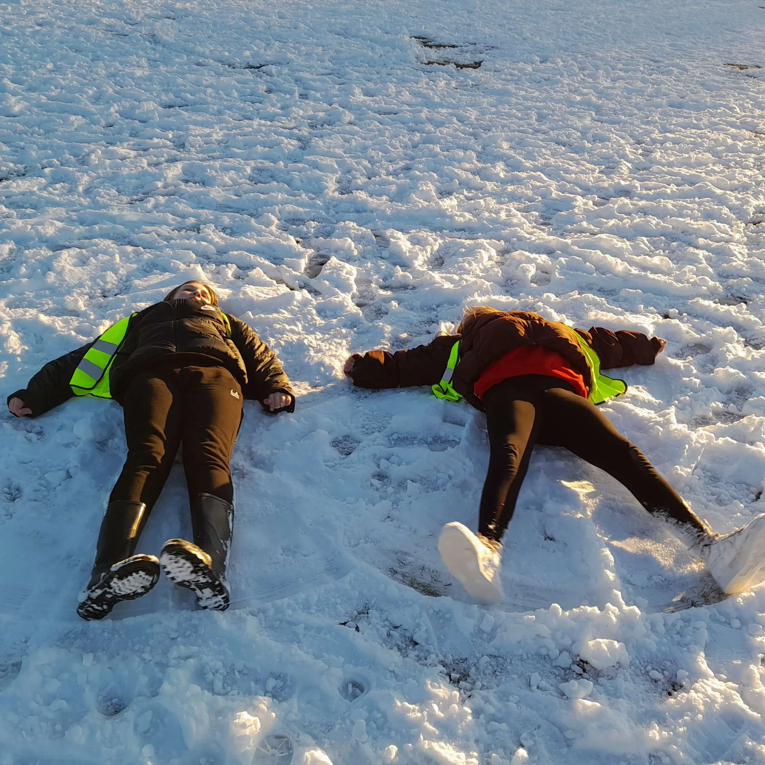 Two children in high-visibility vests making snow angels during an outdoor session at Muirfield After School Club in Aberdeen.