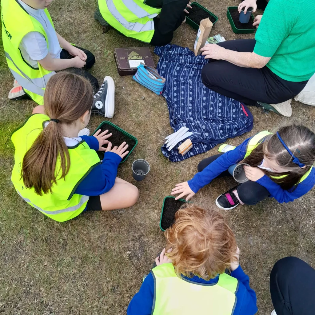 Children in high-visibility vests participating in an outdoor gardening activity at Muirfield Primary School after school club, representing Community Link Childcare’s 25 years of hands-on experience.