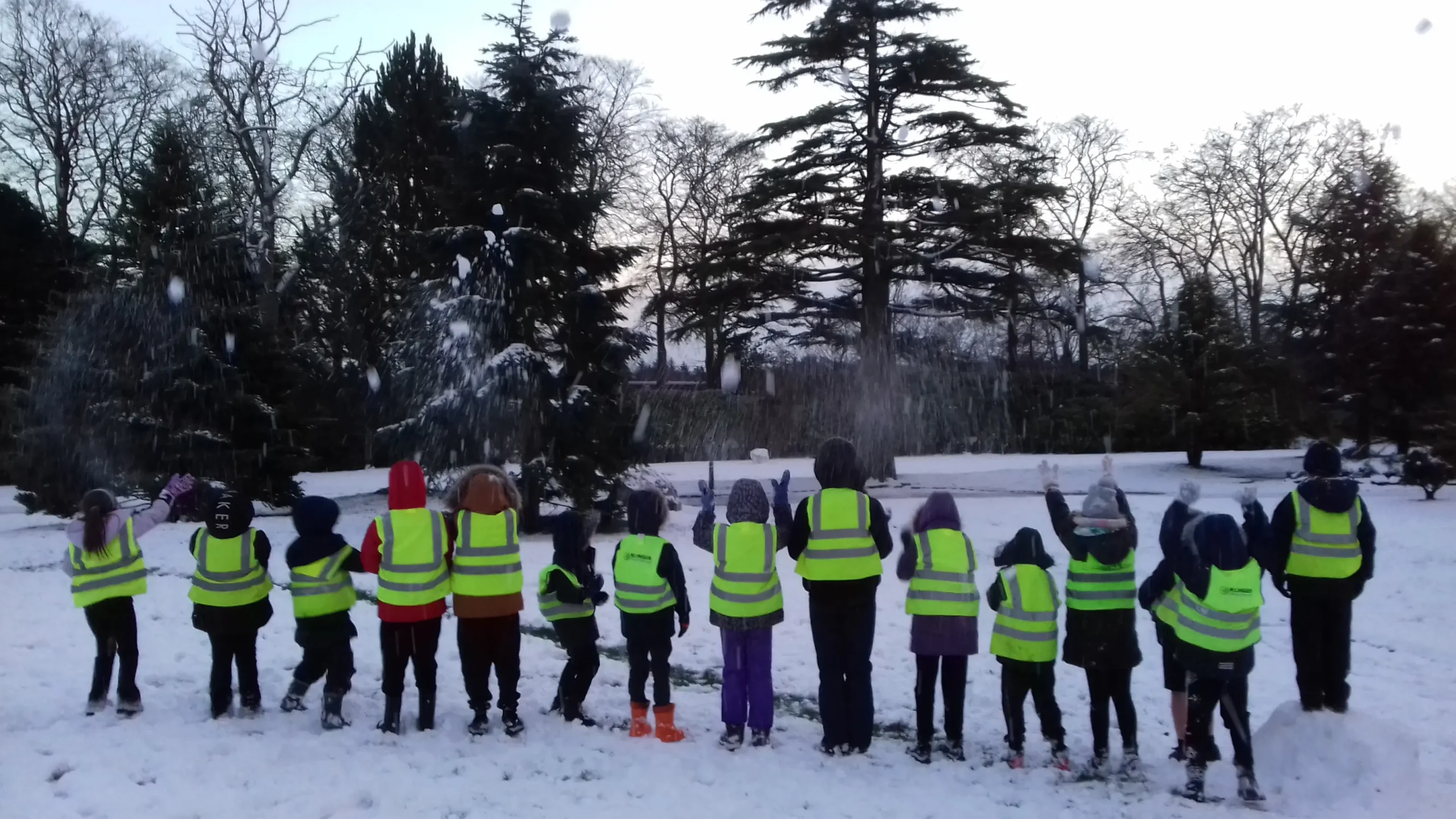 A group of children wearing high-visibility vests playing in the snow during a Trailblazers afterschool club session at Hazlehead Park in Aberdeen.